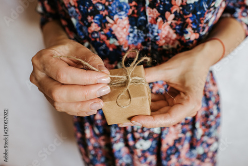 Woman hold gift in hand. Holiday present. Box with surprise. Happy celebration event. Kraft paper packaging. Wrapping paper and ribbon. Female hand with box close-up. Handmade congratulation