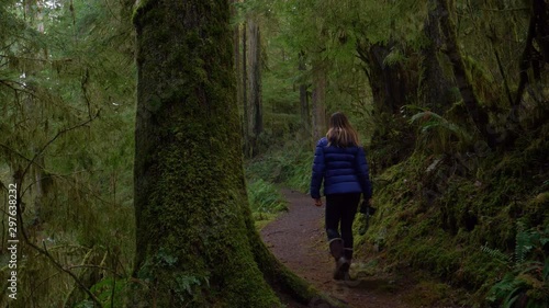 CLOSE UP: Unrecognizable female photographer treks through the scenic Hoh Rainforest. Young woman strolls along the scenic path leading through the lush Olympic National Forest in rainy Washington. photo