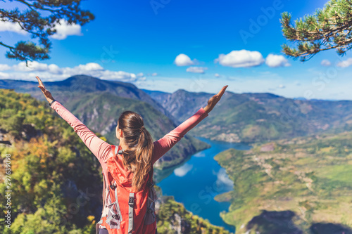 Female backpacker with hands up enjoying the valley view on top of a mountain. Hiking and healthy lifestyle concept. photo