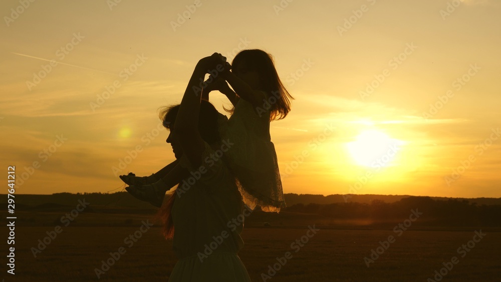 little daughter riding on mom's shoulders in sunset, walk in park in summer. young family with baby, in field.