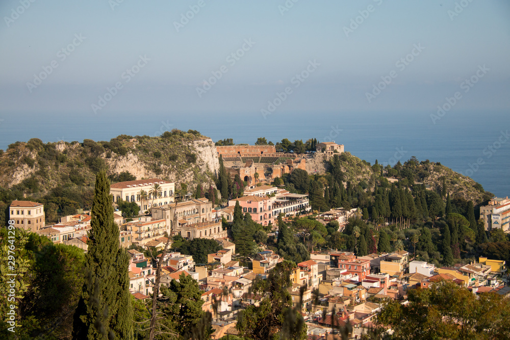 Beautiful panorama from mountain top to a small mediterranean sicilian town, Taormina, in warm sunset with the sea in the background, Sicily, Italy	