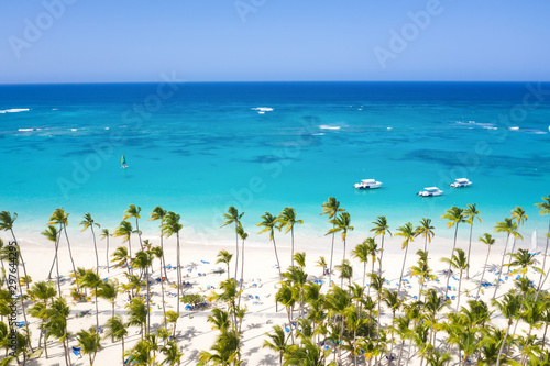 Aerial view from drone on tropical coastline with coconut palm trees, sunbeds and boats floating in caribbean sea