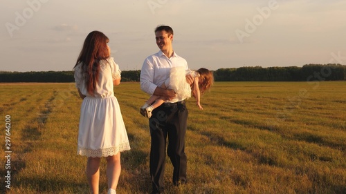 concept of happy childhood. child, dad and mom play in the meadow in the sun. mother, father and little daughter walking in a field in the sun. Happy young family. concept of a happy family.