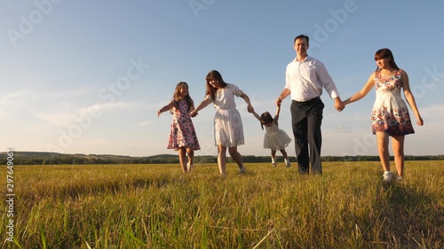 Children, dad and mom play in meadow in sunshine. mother, father and little daughter with sisters walking in field in the sun. Happy young family. concept of a happy family.
