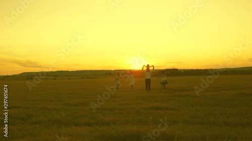 Happy young family with child run across field in sunset light. mother, father and little daughter with sisters walking in park. Children, dad and mom play in meadow in sunshine. © zoteva87