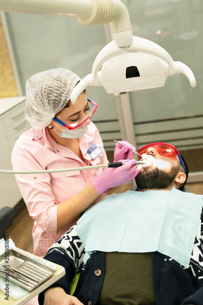 Dentist young woman treats a patient a man. The doctor uses disposable