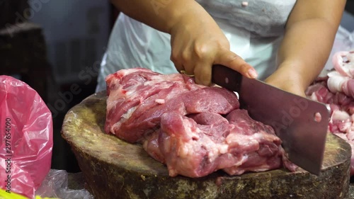 Butcher chopping and cutting meat for sale at a street market, Philippines. Butcher chopping raw meat with a knife on a wooden board in a street market. Butcher hands close up: cutting meet