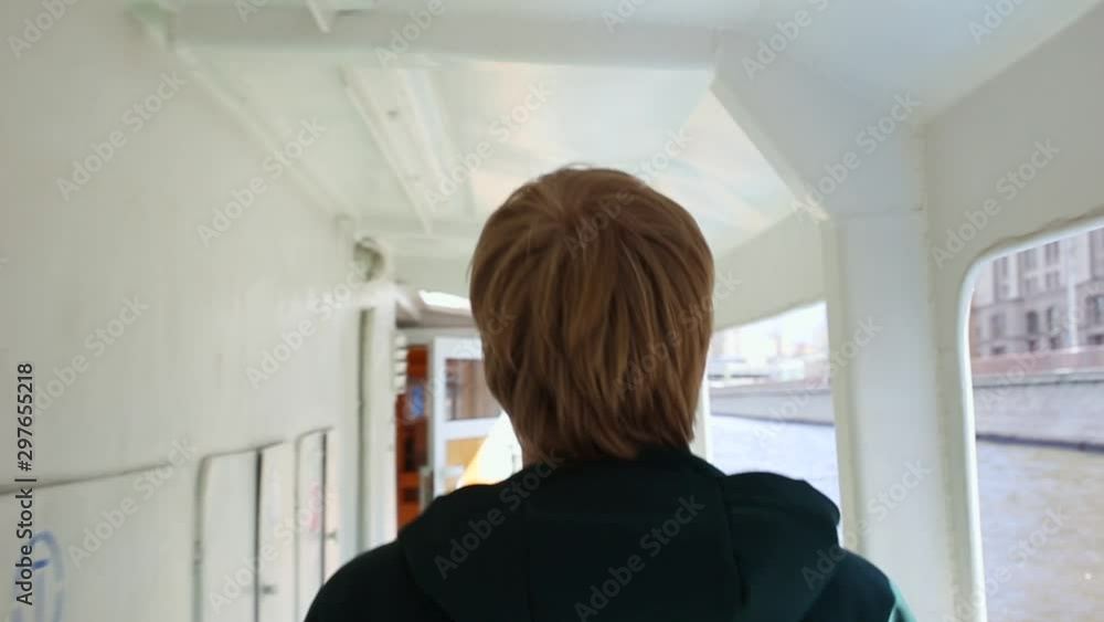 blond man wearing green sweatshirt walks along deck of ship along railing. boat moves along Moscow river on clear sunny day. rear view, close up on male's head and shoulders blond man wearing green sweatshirt walks along deck of ship along railing. boat moves along Moscow river on clear sunny day. rear view, close up on male's head and shoulders