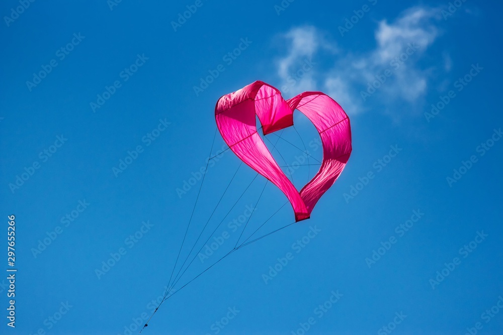 A pink heart-shaped kite flying in the air against a clear blue sky background A pink heart-shaped kite flying in the air against a clear blue sky background