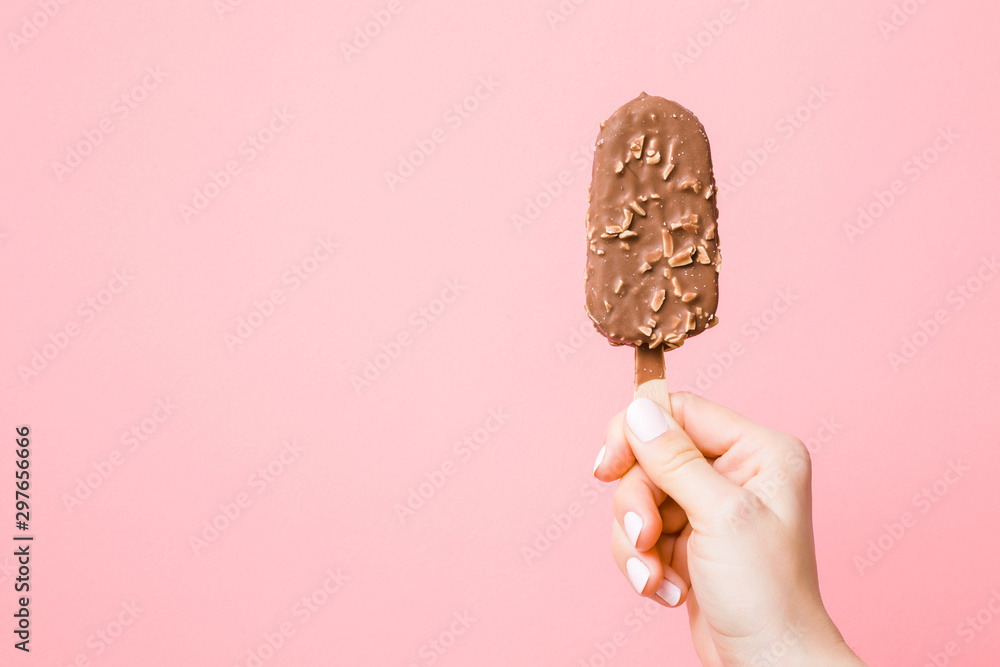 Young woman hand holding ice cream with nuts and chocolate glaze on pastel pink background. Empty place for text, quote or sayings. Point of view shot. Closeup. - obrazy, fototapety, plakaty 