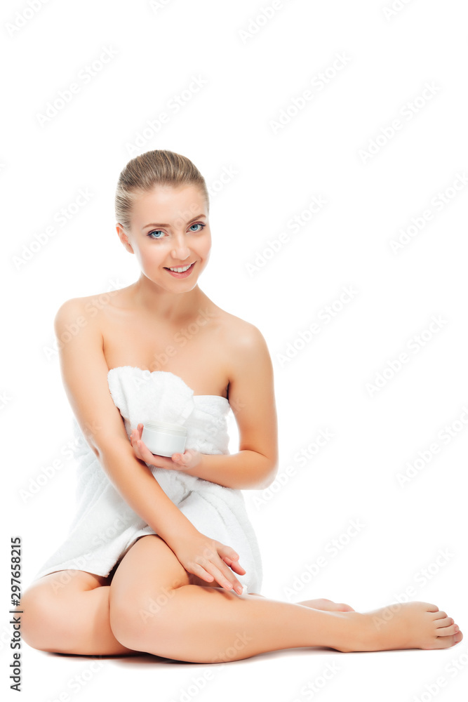 Beautiful girl holding and showing cream for care of skin body. Young woman in towel sitting, on white background. Cosmetics for hydrating and rejuvenating. Beautiful girl holding and showing cream for care of skin body. Young woman in towel sitting, on white background. Cosmetics for hydrating and rejuvenating.
