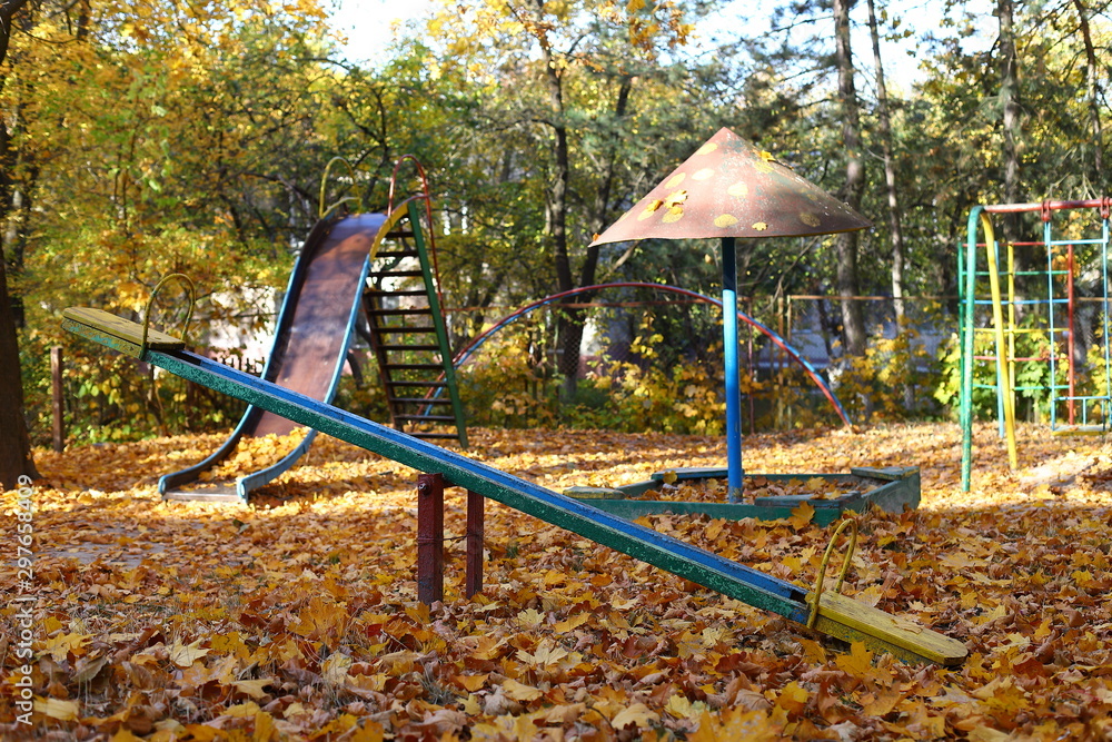 Autumn old playground for children covered with yellow and orange leaves. Old swing and mushroom with sand. Bright autumn day