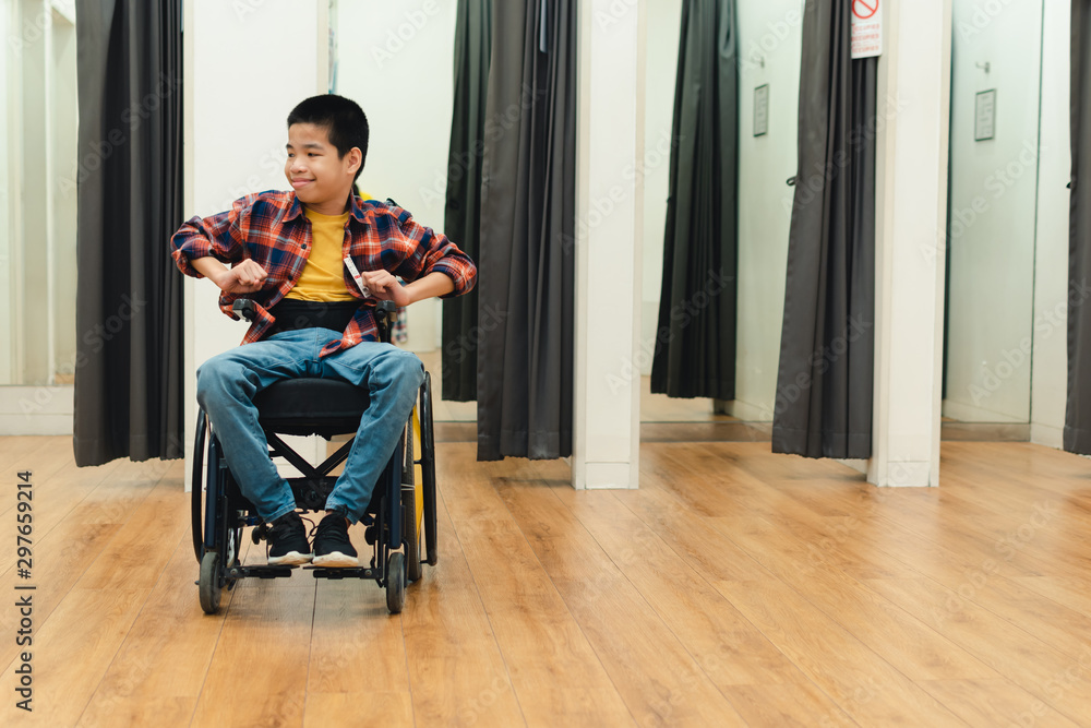 Disabled child on wheelchair having fun shopping for clothes, He is in front of fitting room,Special children's lifestyle,Life in the education age of special need kids,Happy disability kid concept. Disabled child on wheelchair having fun shopping for clothes, He is in front of fitting room,Special children's lifestyle,Life in the education age of special need kids,Happy disability kid concept.