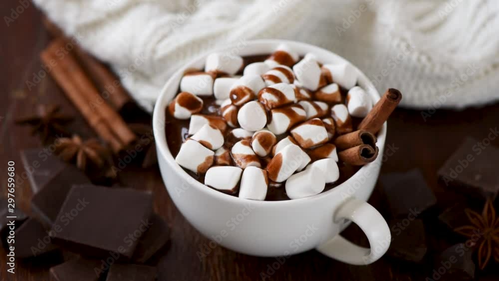 Mug of hot chocolate with marshmallows and cinnamon rotating on wooden table. Hot beverage. Seasonal winter autumn comfort food Mug of hot chocolate with marshmallows and cinnamon rotating on wooden table. Hot beverage. Seasonal winter autumn comfort food