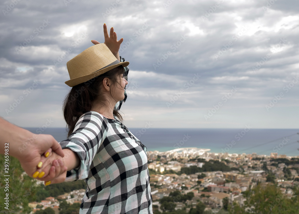 Young woman tourist holds a male hand and holds a hat. follow me