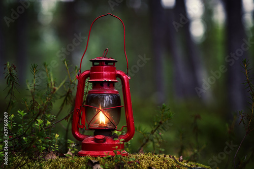 Mystical scene with old red hurricane camping kerosene lantern in forest. Mysterious night in event forest. Magic lantern lighting. dark tone. Summer season. copy space
