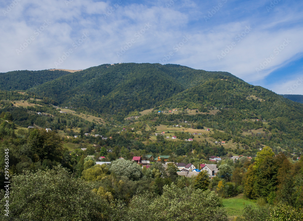 Fototapeta premium Mountain forest green landscape with houses and a far village.