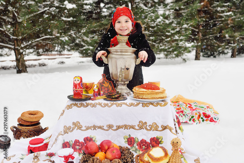 child girl in a fur coat and in a scarf in Russian style holding a large samovar in the hands of pancakes with red caviar
