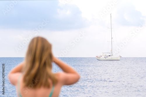 A girl looking at the sea and white yacht in the distance. Young woman stands on the shore and looks through binoculars. Waiting for a lover or groom. Romantic scene with seascape. Holiday romance