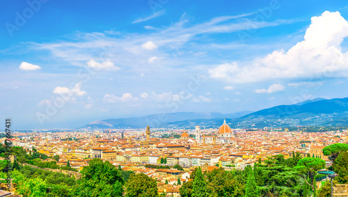 Top aerial panoramic view of Florence city with Duomo Cattedrale di Santa Maria del Fiore cathedral, buildings houses with orange red tiled roofs and hills range, blue sky white clouds, Tuscany, Italy