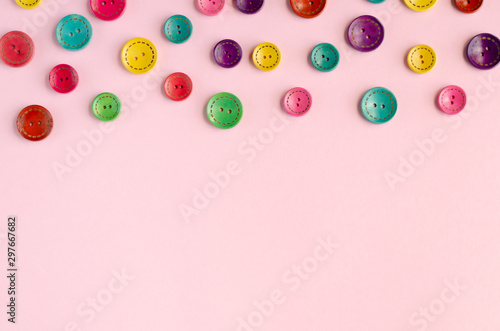 Colored sewing buttons composition on pink background.