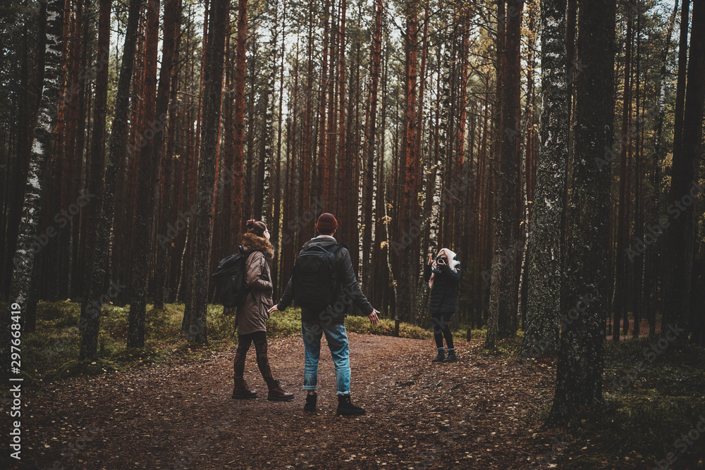 Young blond woman is making a photo of her friends in the deep autumn forest.