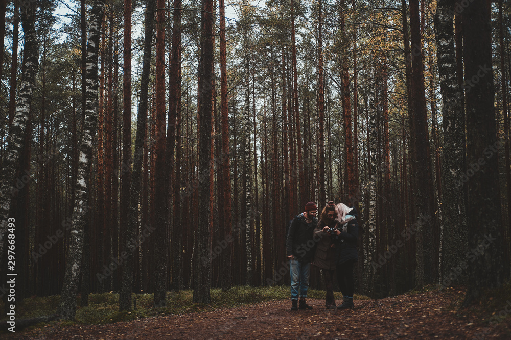 Three friend are watching pictures in photo camera while enjoying their hike in the forest.