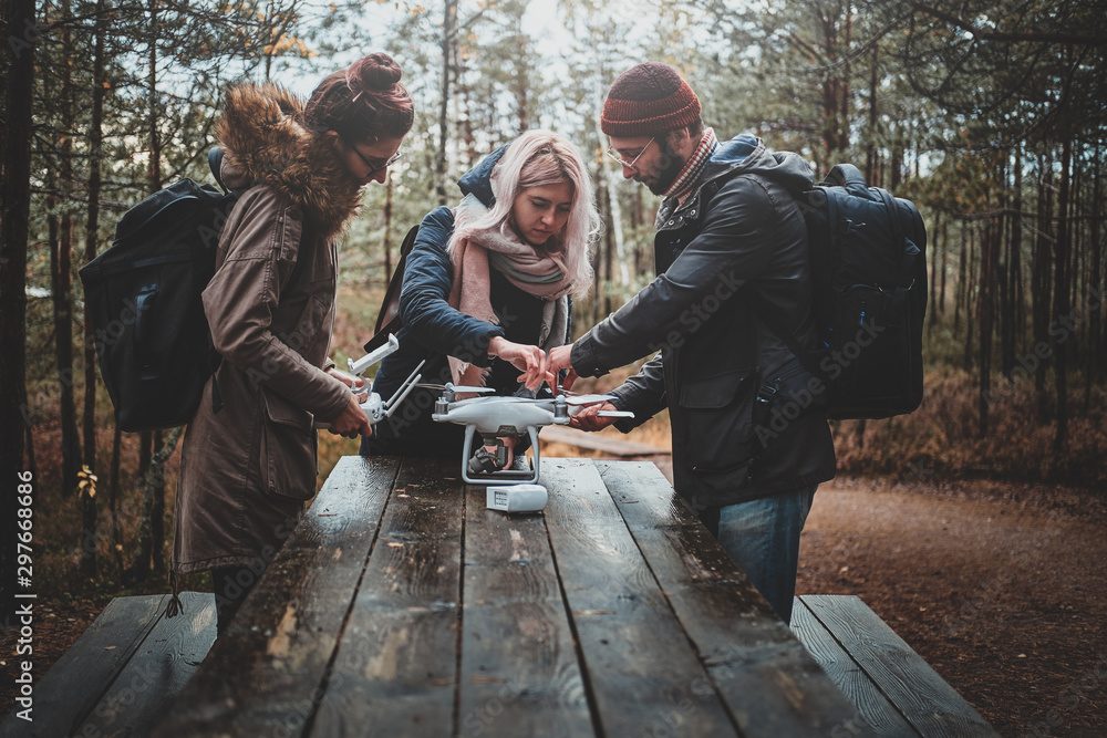 Small group of friends are assembling drone in the forestal park using wooden table. Small group of friends are assembling drone in the forestal park using wooden table.