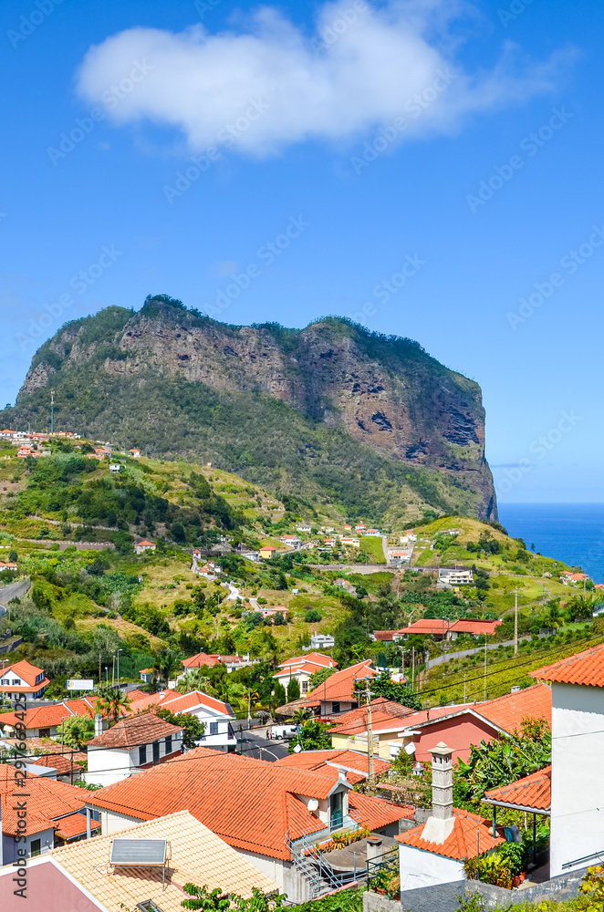Picturesque village Porto da Cruz in Madeira island, Portugal. Houses on the green hills, rock formation, cliff by the Atlantic ocean in the background. Hilly terrain. Portuguese landscapes