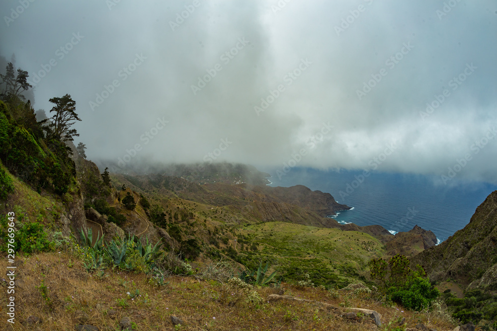 Narrow rural road in the mountains of Parque Natural Majona. Low wet clouds hanging over the green slopes. View of the north-eastern part of La Gomera island. Canary Islands, Spain