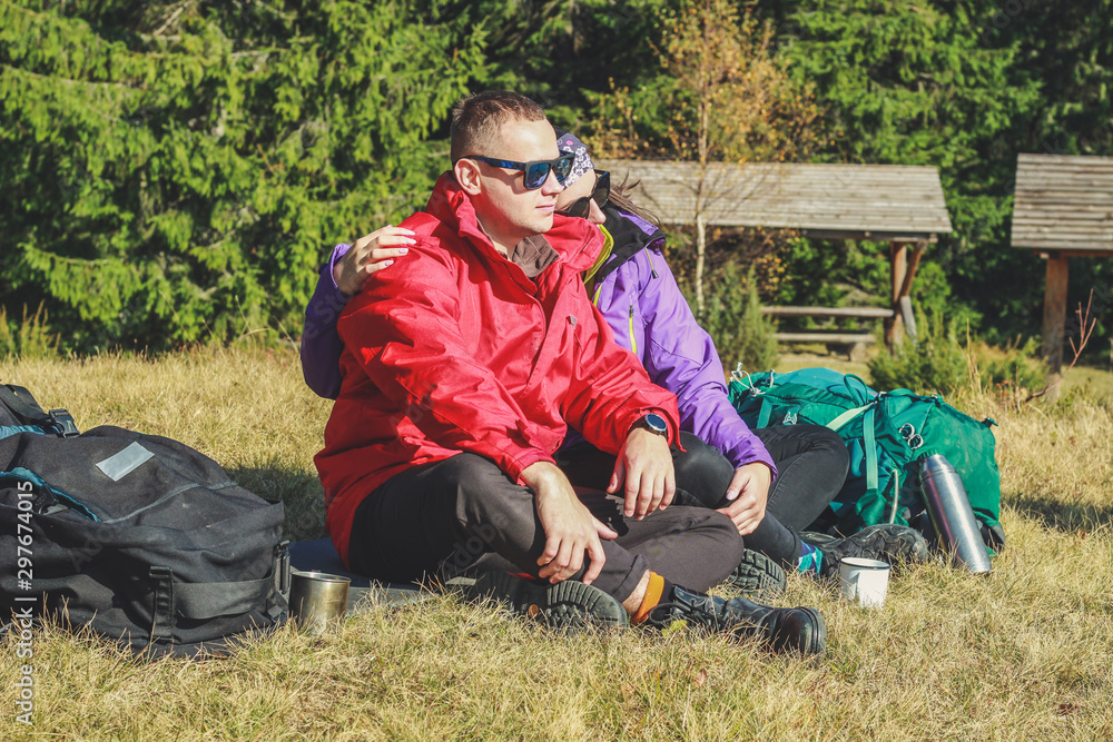 Fototapeta premium Girl and man hikers in mountains. They drink tea and coffee on top. Embrace. Campaign. Ukrainian Carpathian Mountains. Traveling in Ukraine.