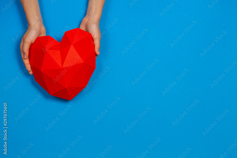 Obraz premium Hands holding red polygonal paper heart shape on light blue background
