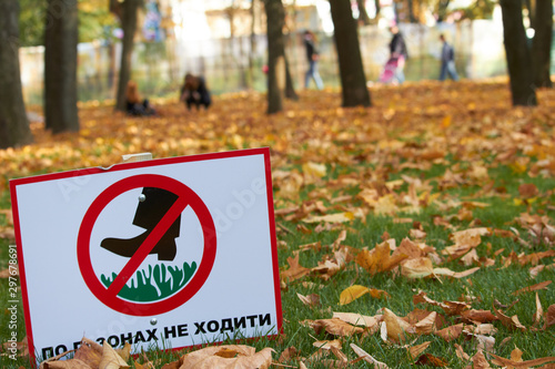 Green lawn with fallen maple leaves and a sign with the inscription in Ukrainian: do not walk on the lawns