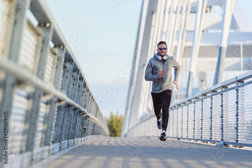Attractive fit man running fast along big modern bridge. Exercising, Jogging, Sport, Winter. Male athlete running.