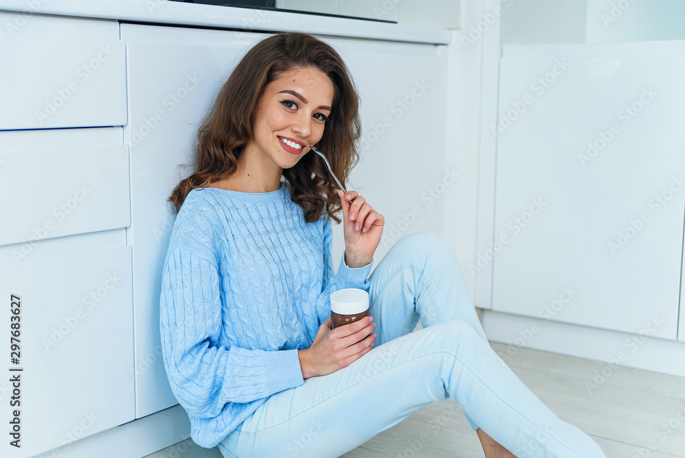 Pretty exuberant young woman in casual stylish clothes enjoying tasty chocolate cream and looking at camera with cute smile in the cuisine interior. Pretty exuberant young woman in casual stylish clothes enjoying tasty chocolate cream and looking at camera with cute smile in the cuisine interior.