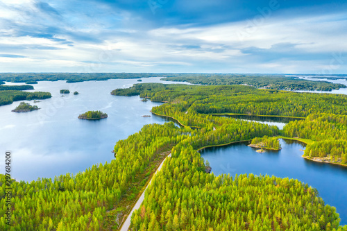 Aerial view of road between green summer forest and blue lake in Finland