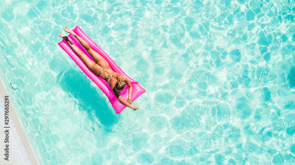 Attractive young woman in bikini relaxes in the pool with a floating pink mattress
