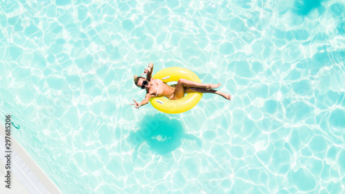 Beautiful young woman in swimming pool aerial top view from above. Girl in bikini relaxes and swims on inflatable ring has fun in water on family vacation © F8  \ Suport Ukraine