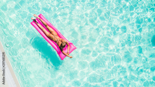 Attractive young woman in bikini relaxes in the pool with a floating pink mattress