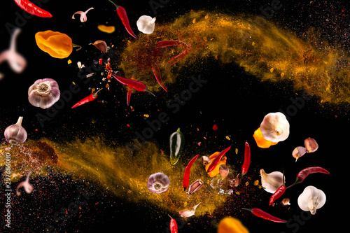 Fototapeta Naklejka Na Ścianę i Meble -  Hot red pepper, garlic, different spices powder flying on a black background Motion freeze photo composition