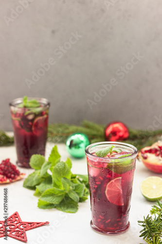 Cold purple cocktail or lemonade with fruit juice, lime slices, mint leaves, pomegranate and ice cubes on light grey background. Christmas or New Year concept.