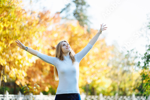 SHappy young blonde woman enjoying autumn breeze in the park. The sun is shining.