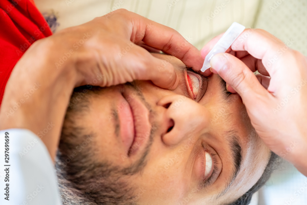 Doctor giving his patient eye drops in his eyes Doctor giving his patient eye drops in his eyes