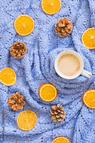 Winter mood composition. Cup of coffee, knitted blue blanket, dry oranges, pine cones. Flat lay, top view