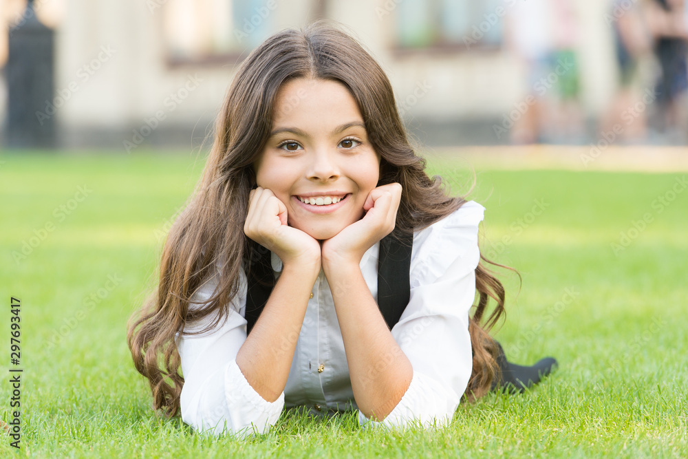 Future woman. Happy girl back to school. Small girl relax on green grass. Little girl smile with long brunette hair. Cheerful girl child in formal school uniform outdoor Future woman. Happy girl back to school. Small girl relax on green grass. Little girl smile with long brunette hair. Cheerful girl child in formal school uniform outdoor