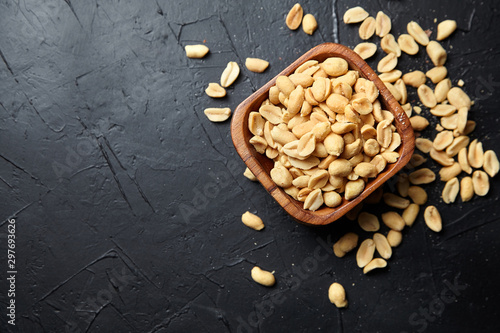 Photography Wooden bowl with roasted peeled peanuts, salty beer snack on dark background wit