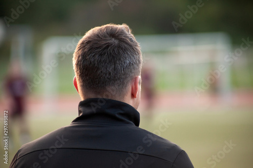 Young football, soccer coach watches the team during the game, rear view