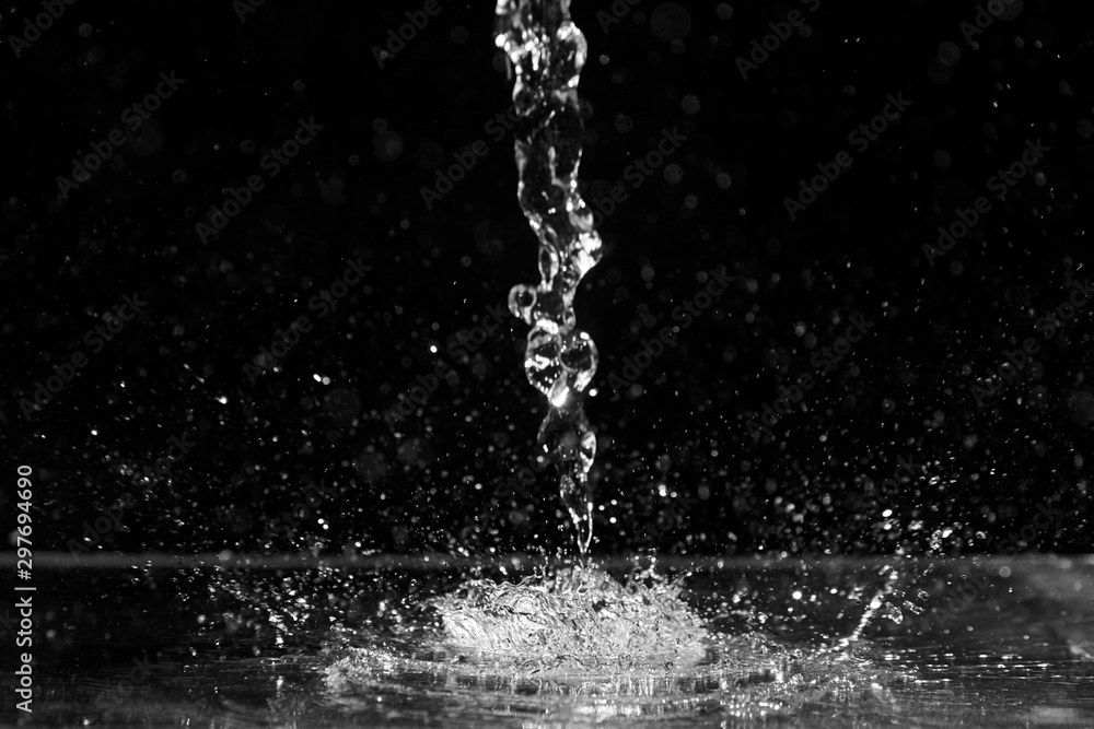 Fototapeta Wodny pluśnięcie na czarnym tle. Strumień i krople przejrzystego płynu. Wlewając przezroczystą wodę