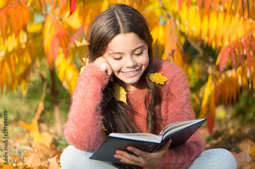 Her hobby is reading. Cute small child reading book on autumn day. Adorable l...