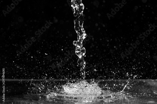 Water splash on black background. Jet and drops of clear liquid. Pouring transparent water